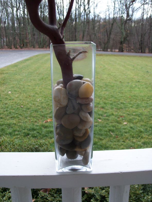 The branches are set in tall square vases with neutral river rocks